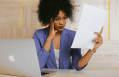 Young Black woman does paperwork with laptop