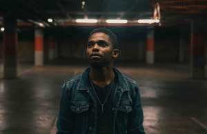 black man in black t shirt with denim jacket standing in dark empty parking garage