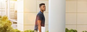 Man walking close to a building holding a notebook.