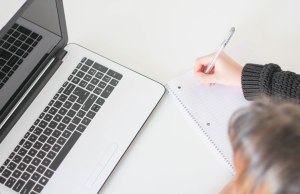 woman writing with laptop and paper