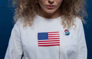 woman with curly hair wearing white sweatshirt with american flag symbol