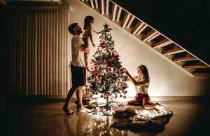 man holding little girl by christmas tree with woman on the floor