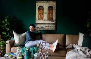 man with dark hair in green sweater on brown leather couch