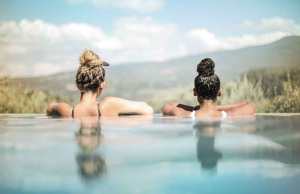 two girls in blue water looking out into mountain landscape.
