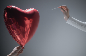 person holding needle towards red hear balloon