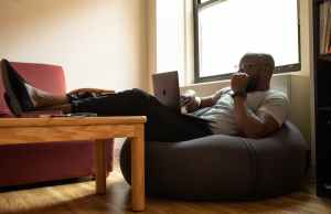 Man sitting on a beanbag on his laptop with his legs resting on a table.