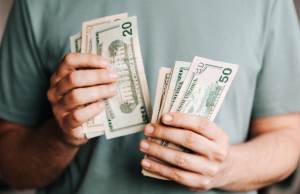 man-holding-dollar-bills-in-hands-with-green-shirt