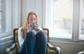 White woman sitting in armchair drinking tea with her eyes closed