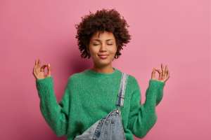 Woman standing in front of a pink/purple background meditating.