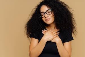 Touched woman with glasses holding her hands to her chest